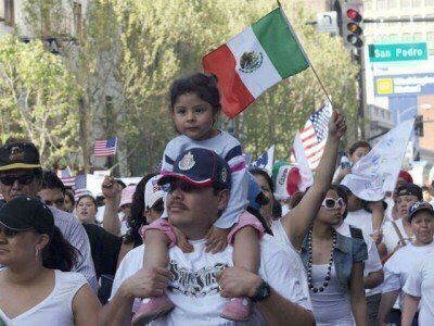 Child on shoulders of man wearing a cap in a crowd of people waving United States and Mexico flags 