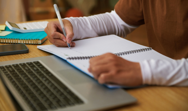 photo of student's hands taking notes beside a laptop keyboard