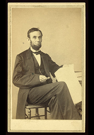 Portrait by Alexander Gardner, photographer, of Lincoln, seated, holding glasses and paper, taken August 9, 1863.
