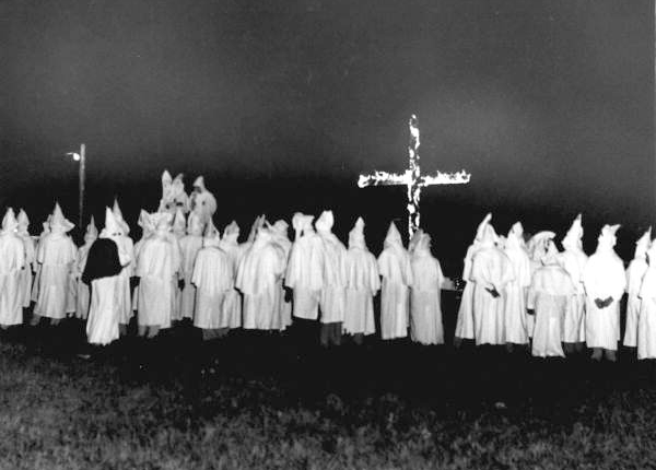 Group of ku klux klan members dressed in white robes burning a cross in a field at night,
1956.
