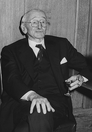 Black and white photo of Friedrich August von Hayek, Professor of Economic Science at LSE 1931-1950, won Nobel prize for Economic Sciences in 1974. He is sitting at a table, one hand on his knee, the other holding a glass.