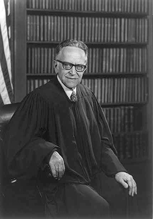 Harry A. Blackmun wearing judicial robes, three-quarter seated portrait in front of bookcase and flag by Robert S. Oakes, photographer, 1976.