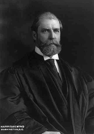 Justice Charles Evans Hughes seated wearing judicial robes, half-length portrait by Harris and Ewing.