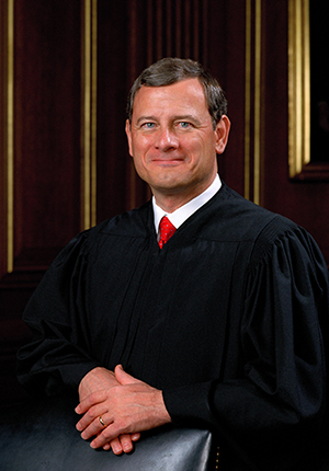 Justice John G. Roberts, three-quarters portrait, standing with arms folded over the back of a chair, wearing judicial robes.