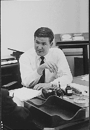 Patrick Buchanan, Presidential Aide, 1969, seated at a desk in
conversation with someone off frame.