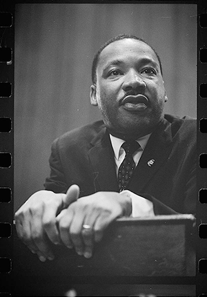 Film negative of head-and-shoulders-portrait-of Martin-Luther-King-leaning-on-a-lectern.