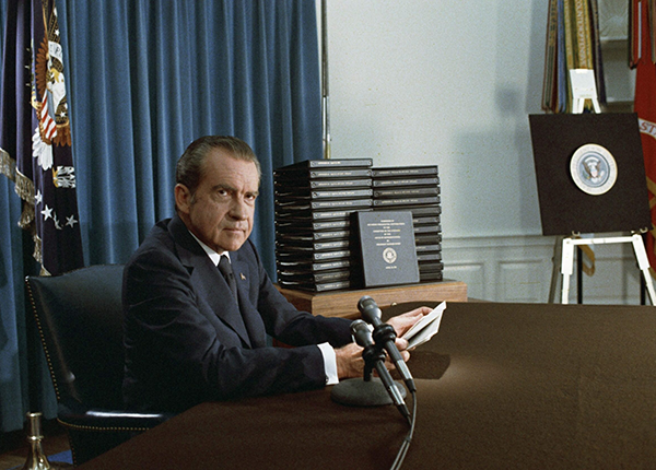 Richard Nixon sitting at desk with microphone during press conference releasing the transcripts of the White House Tapes, 1974.