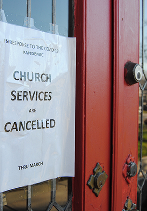 Doors of a building with piece of white paper taped to the glass with the following words in black text, 'In response to the Covid-19 pandemic church services are canceled thru March.