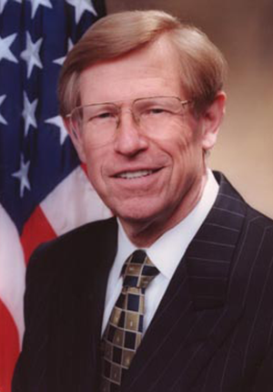 Theodore Olson, head-and-shoulders portrait, seated in front of U.S. flag.