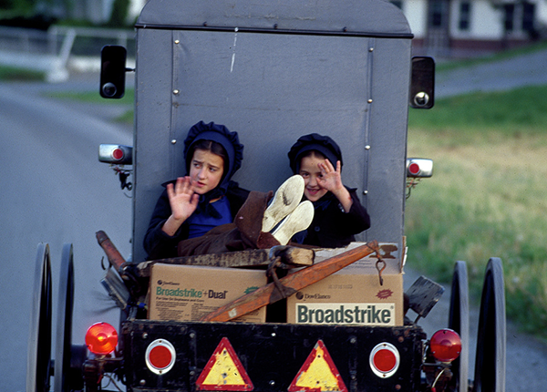 Two Amish girls in back of a buggy with wooden boxes on a paved road by Carol Highsmith, photographer.